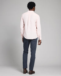Man wearing a light pink shirt and dark blue pants on a gray background
