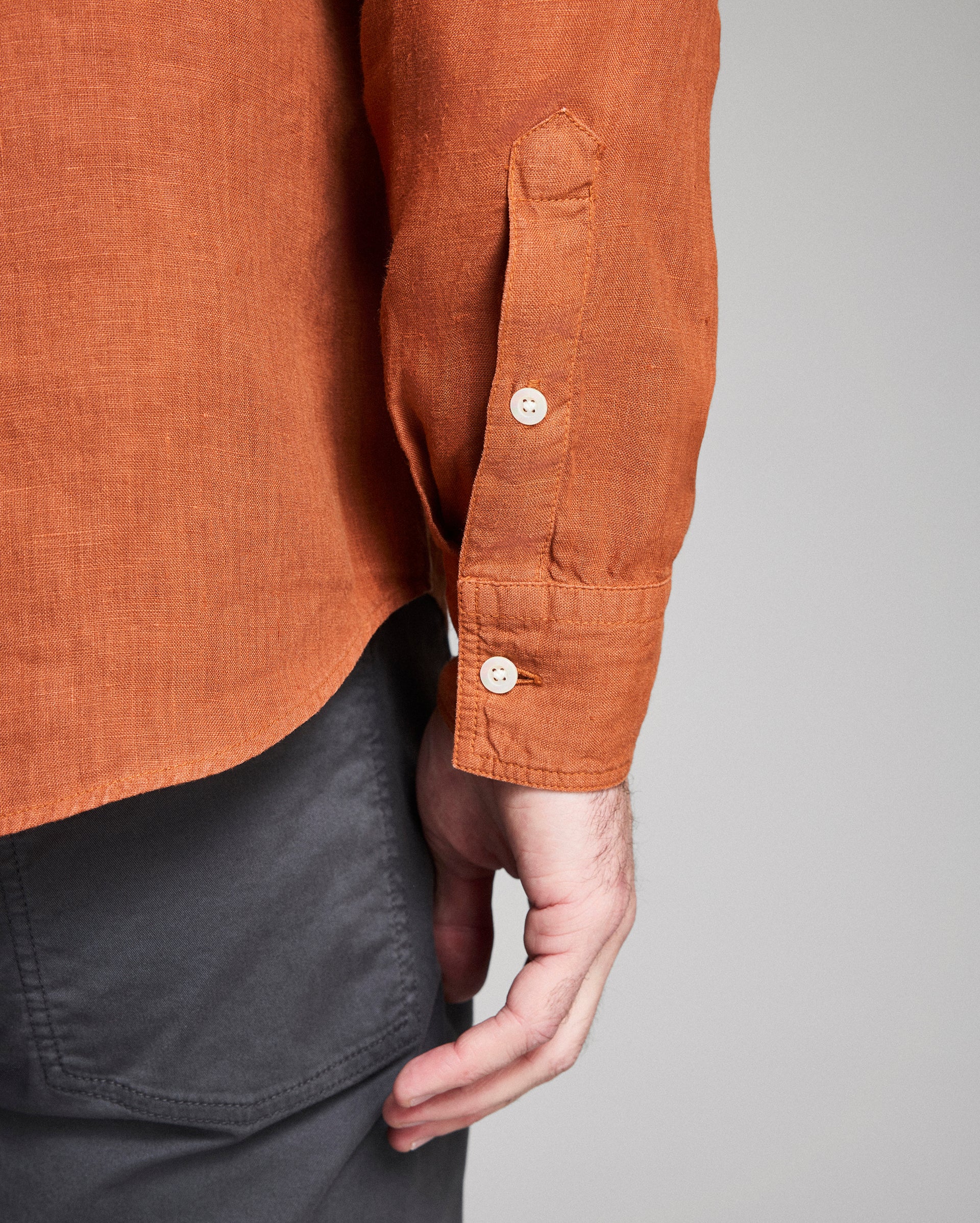 Close-up of a person wearing a brown shirt with rolled-up sleeves on a gray background