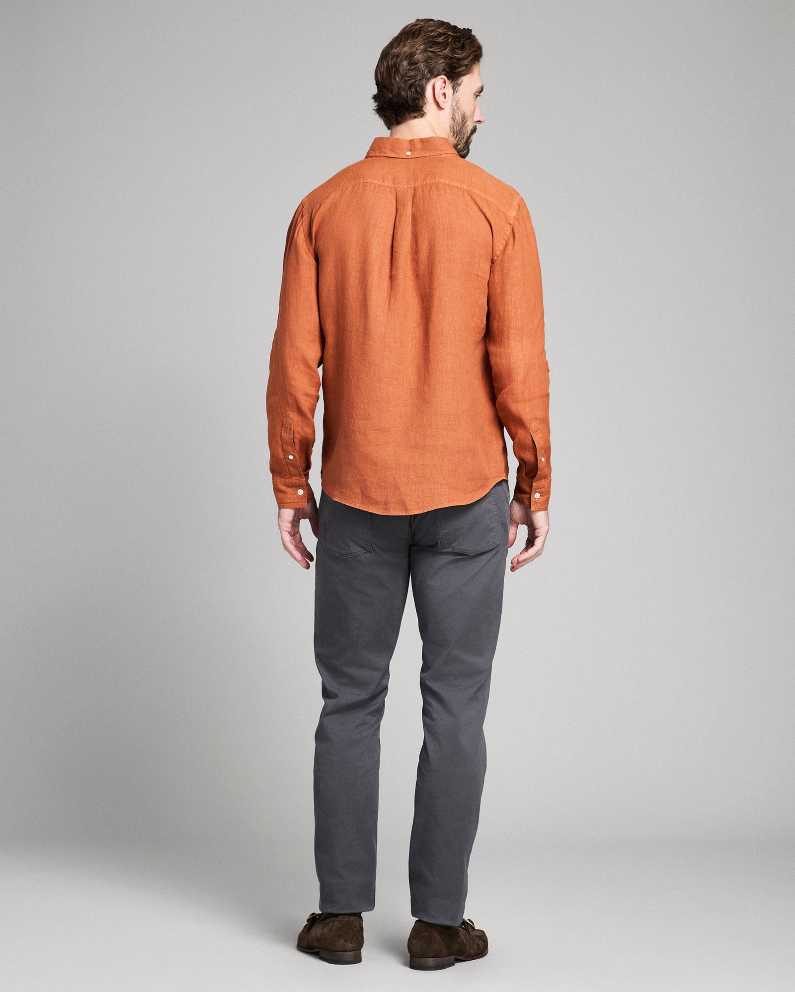 Man wearing a brown shirt and gray pants on a plain background