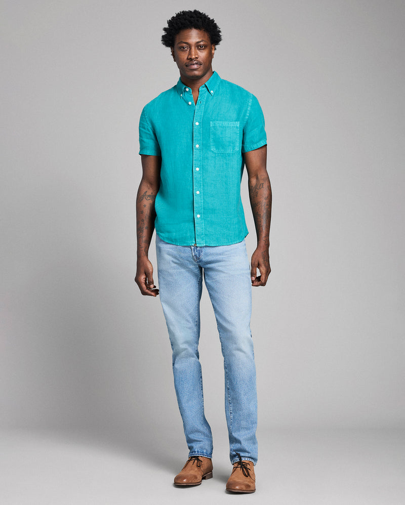 Man wearing a teal button-up shirt and light blue jeans against a gray background Alternate