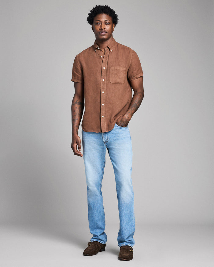 Man wearing a brown shirt and light blue jeans against a gray background