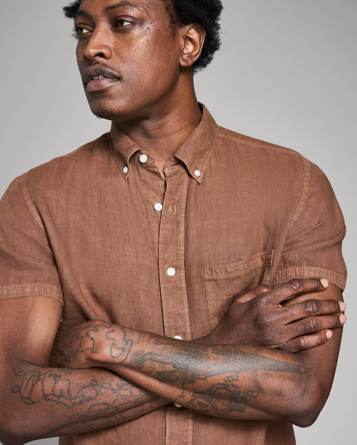 Man wearing a brown shirt with tattoos on his arms against a gray background