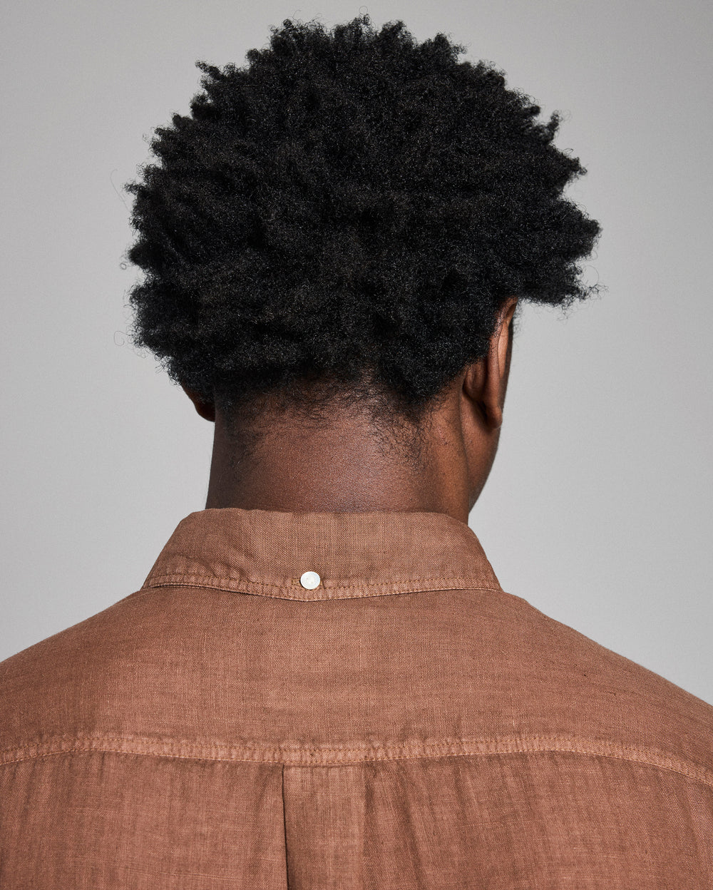 Person wearing a brown shirt with a plain background