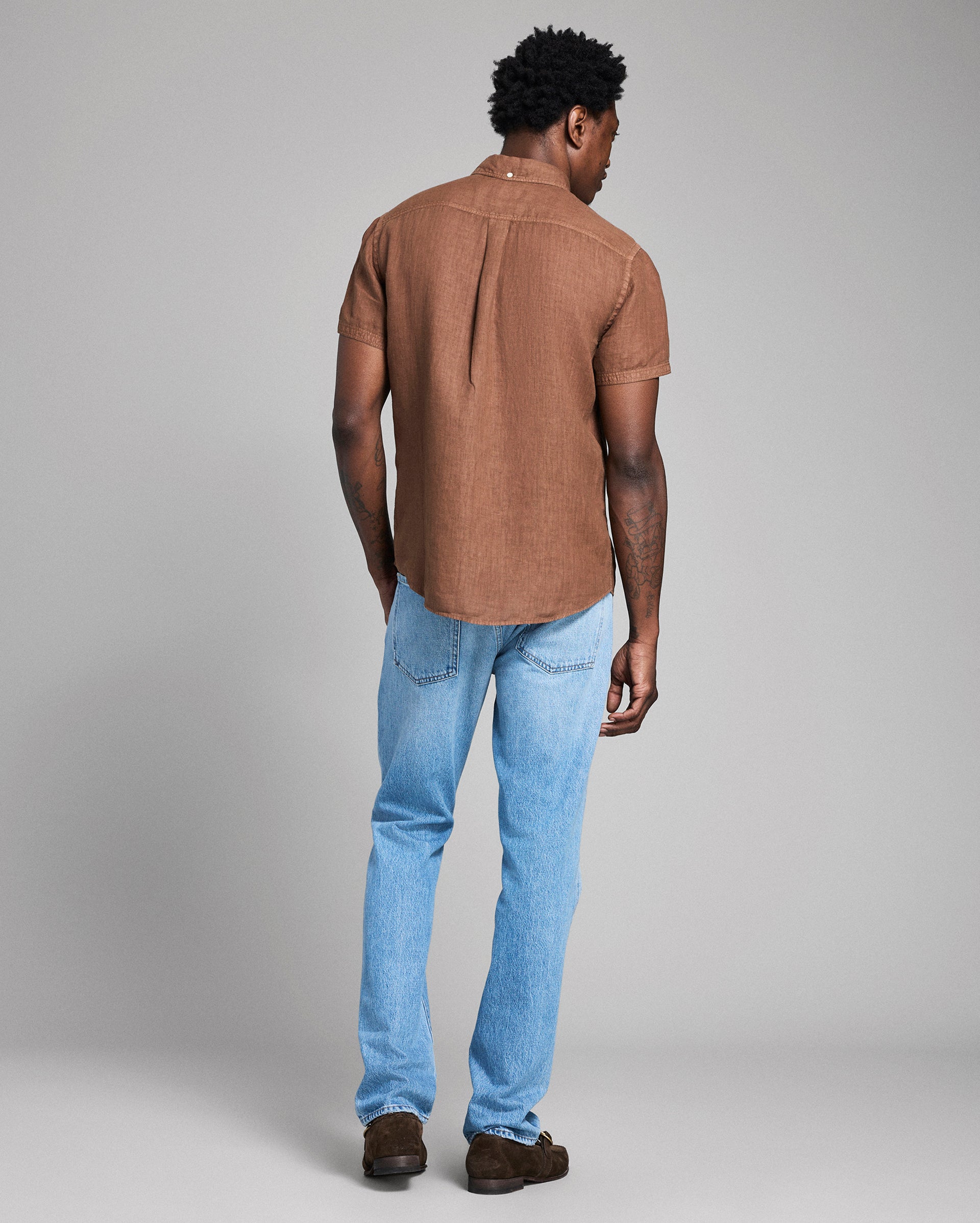 Man wearing a brown shirt and blue jeans against a gray background