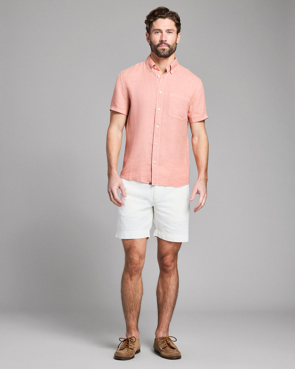 Man wearing a pink shirt and white shorts against a gray background