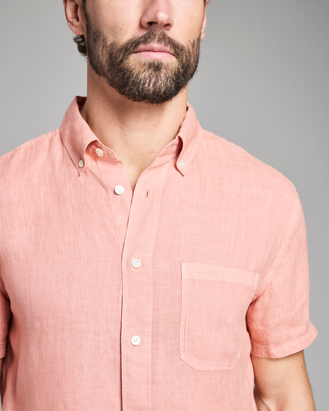 Man wearing a pink short-sleeve shirt against a gray background