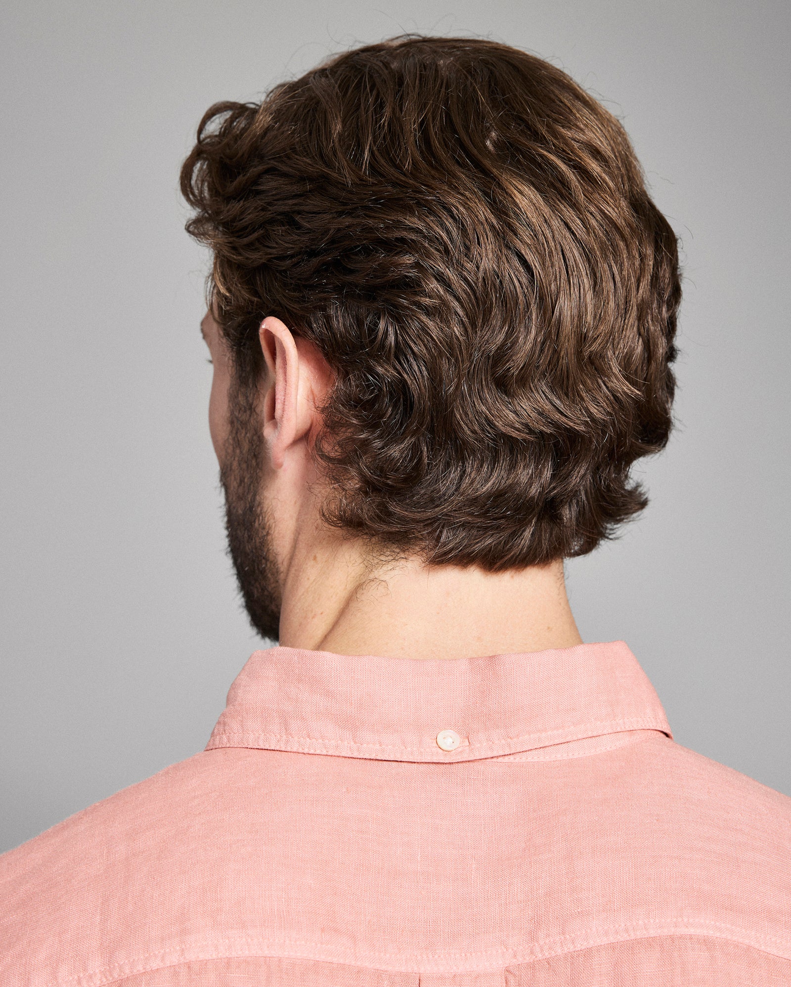 Back view of a person with styled hair wearing a pink shirt on a gray background