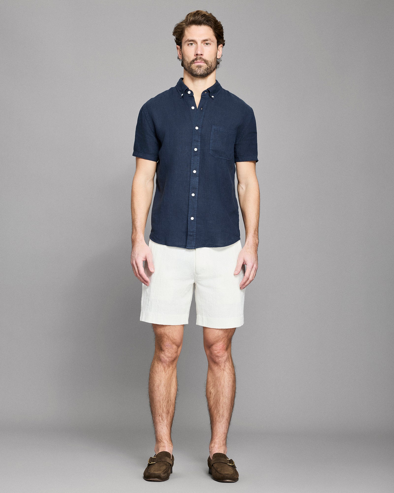 Man wearing a navy button-up shirt and white shorts against a gray background