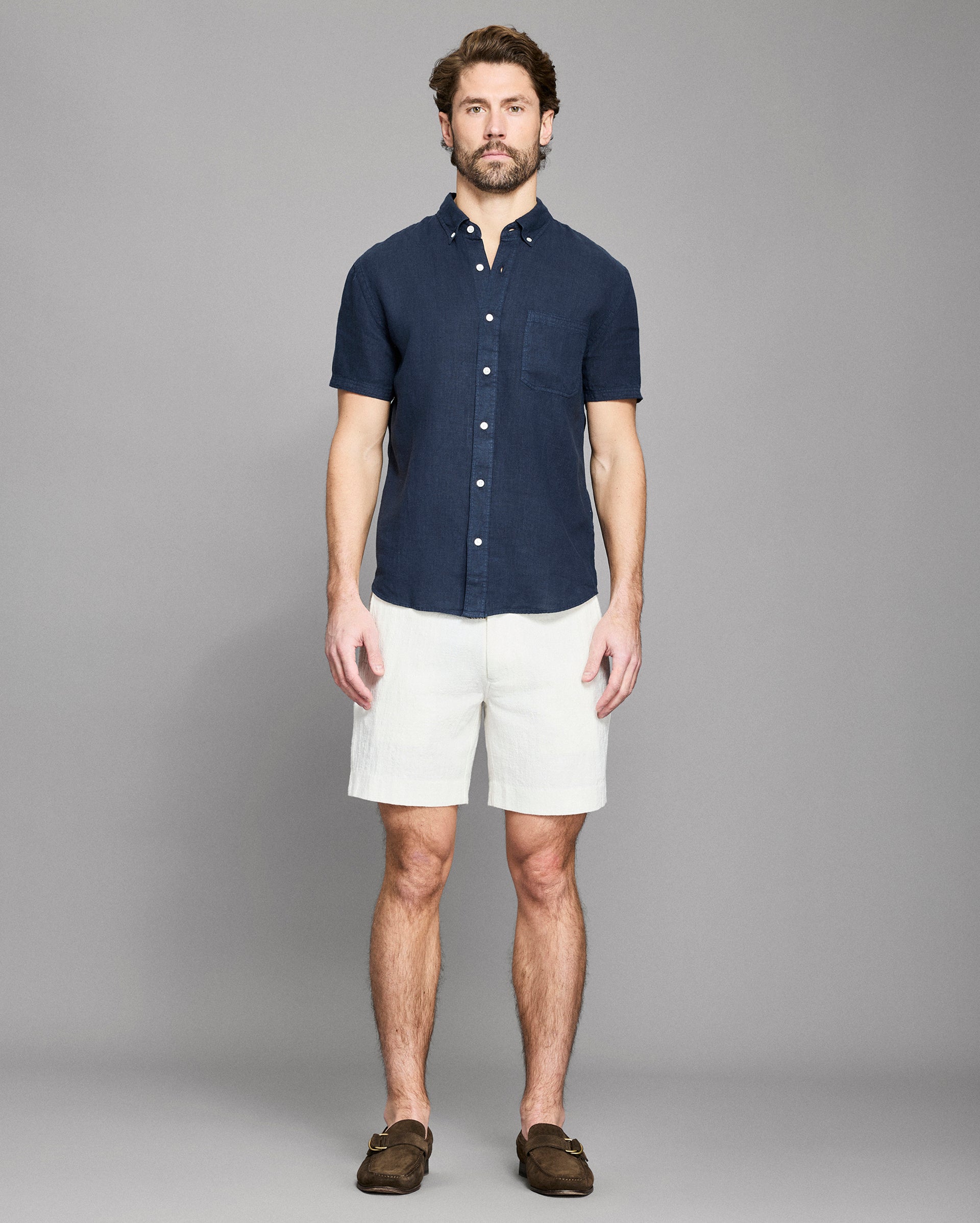 Man wearing a navy button-up shirt and white shorts against a gray background