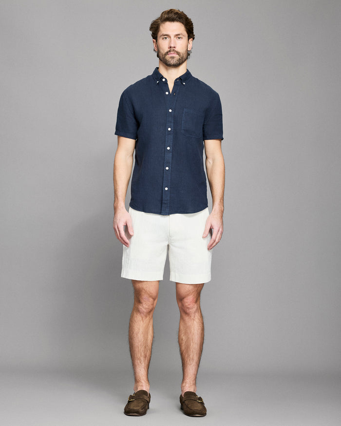 Man wearing a navy button-up shirt and white shorts against a gray background