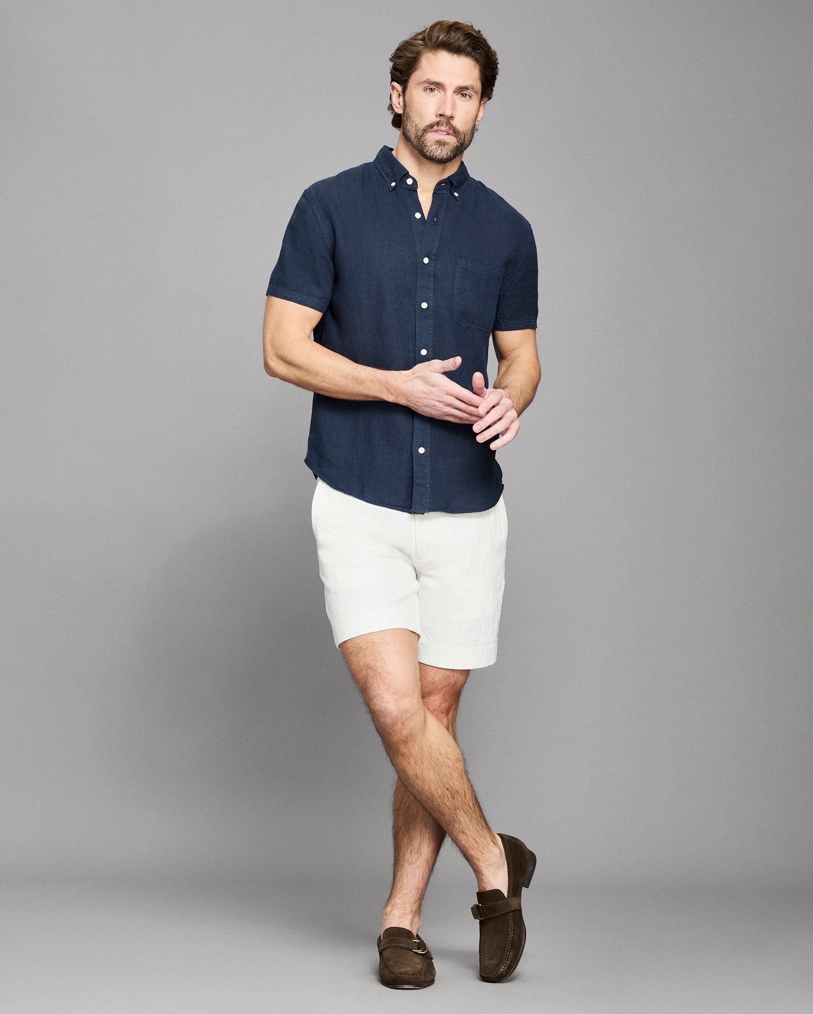 Man wearing a navy button-up shirt and white shorts on a gray background