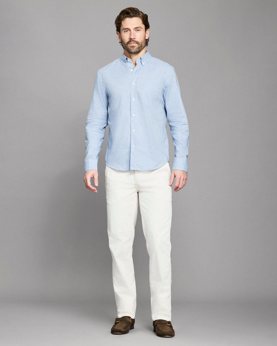 Man wearing a light blue shirt and white pants on a gray background