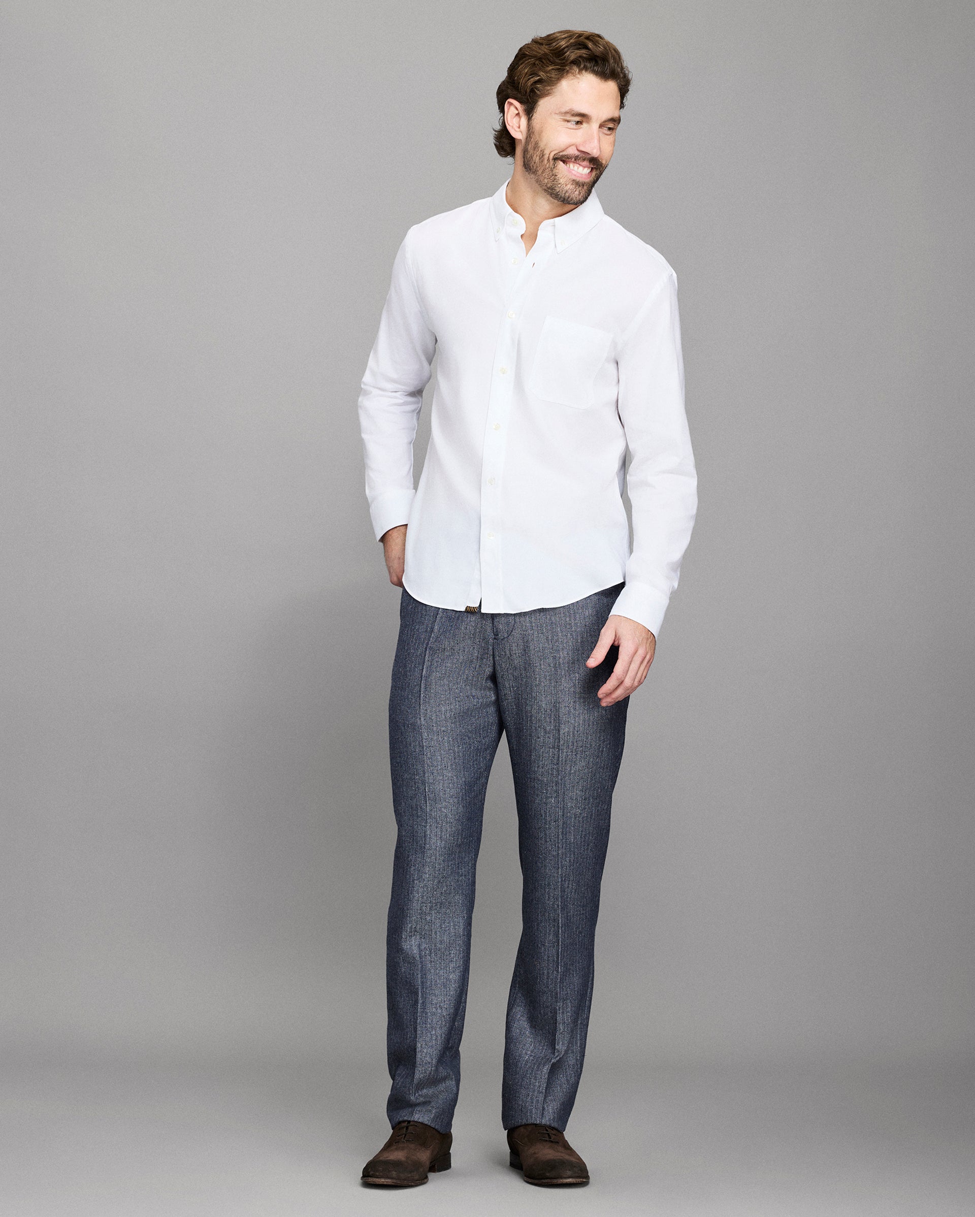 Man wearing a white shirt and dark pants against a gray background
