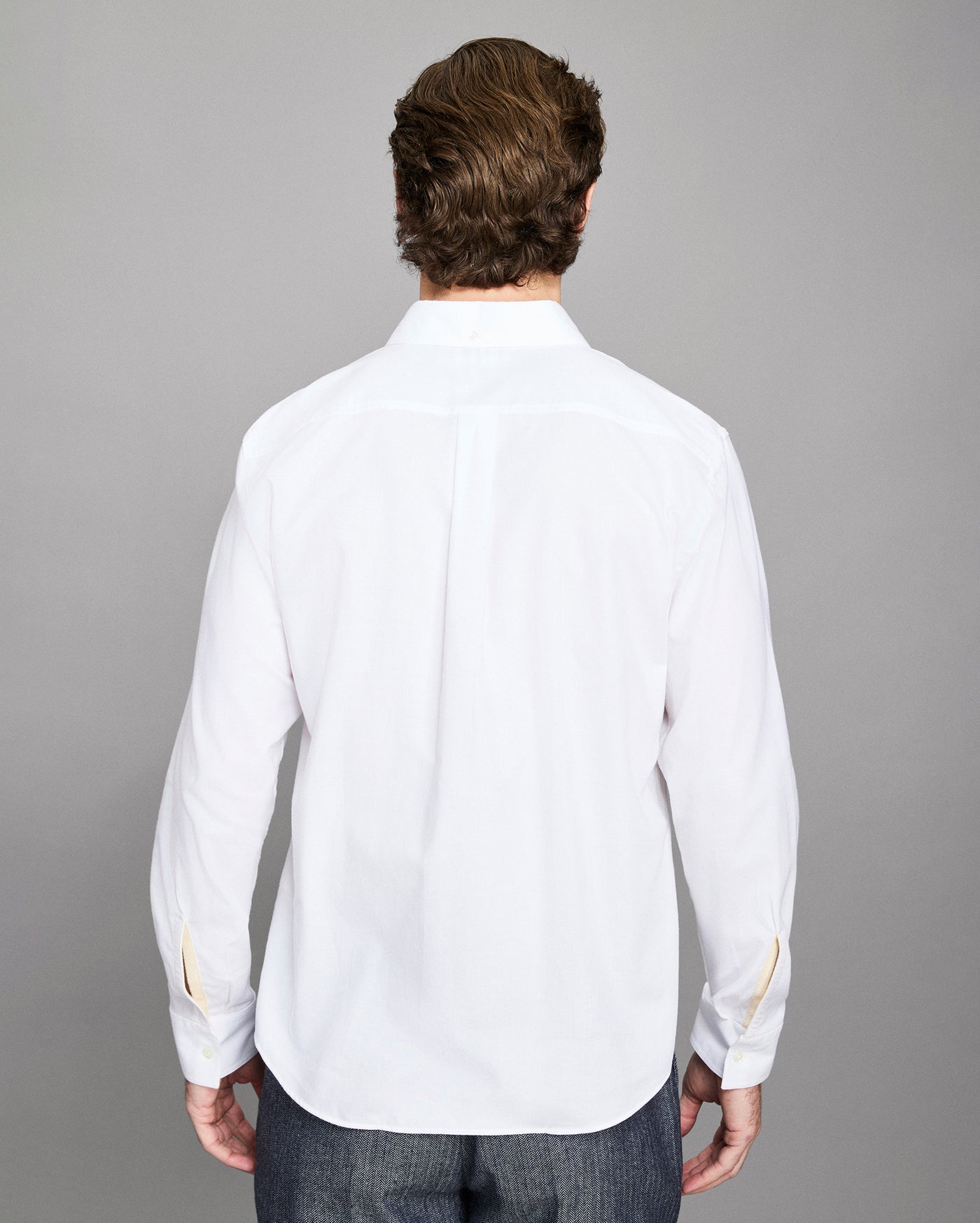 Man wearing a white dress shirt with gold trim on a gray background