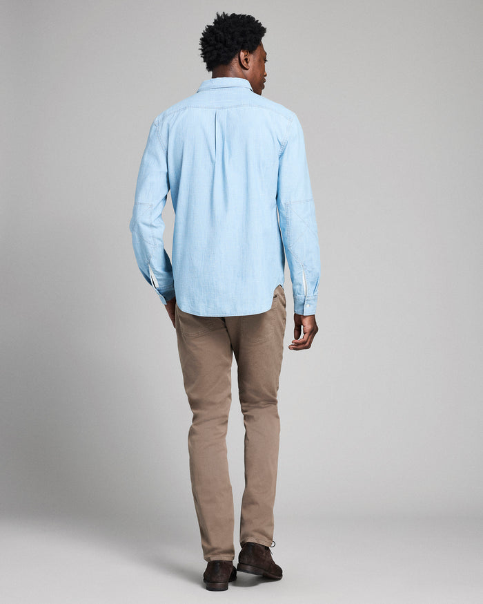 Man wearing a light blue striped shirt and beige pants against a plain background