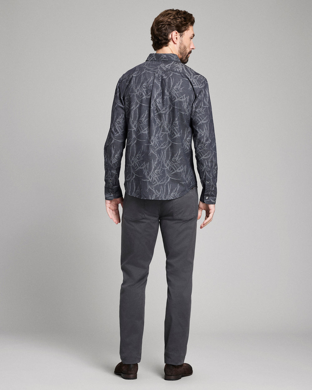 Man wearing a patterned shirt and dark pants on a gray background