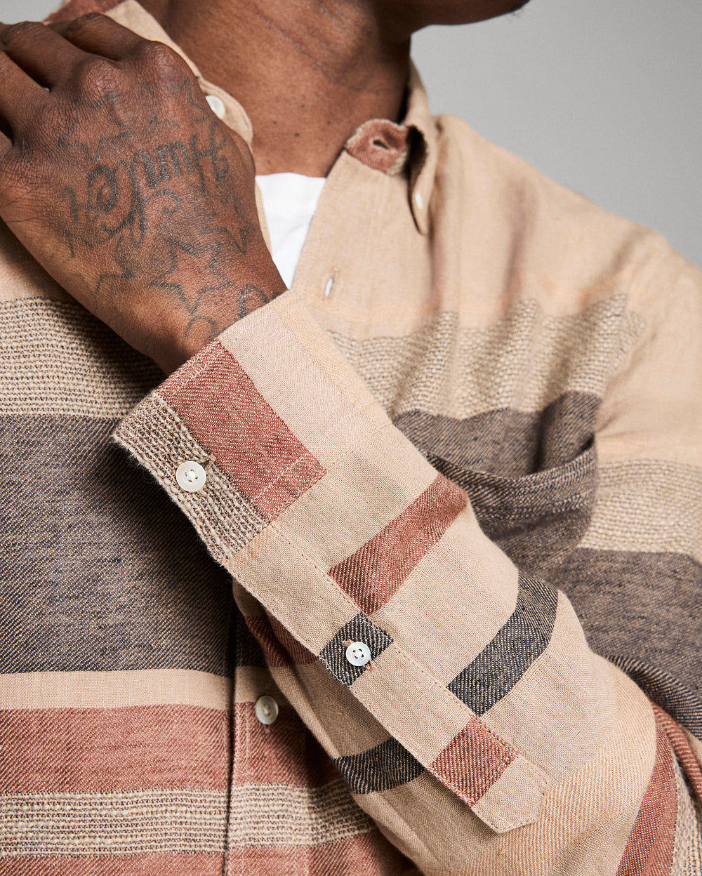 Close-up of a person wearing a plaid shirt with a tattooed arm.