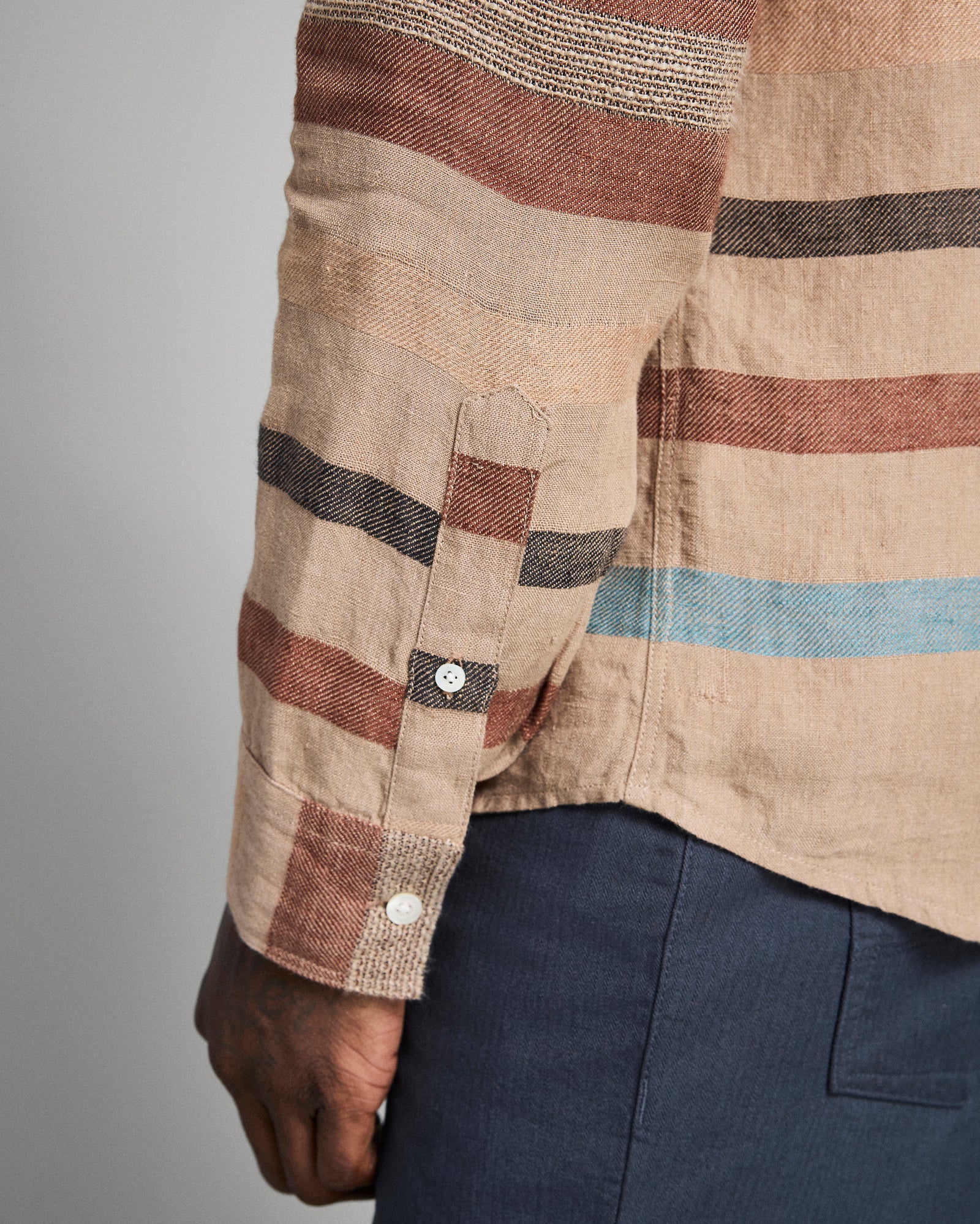 Close-up of a person wearing a plaid shirt with brown, blue, and beige stripes on a gray background.