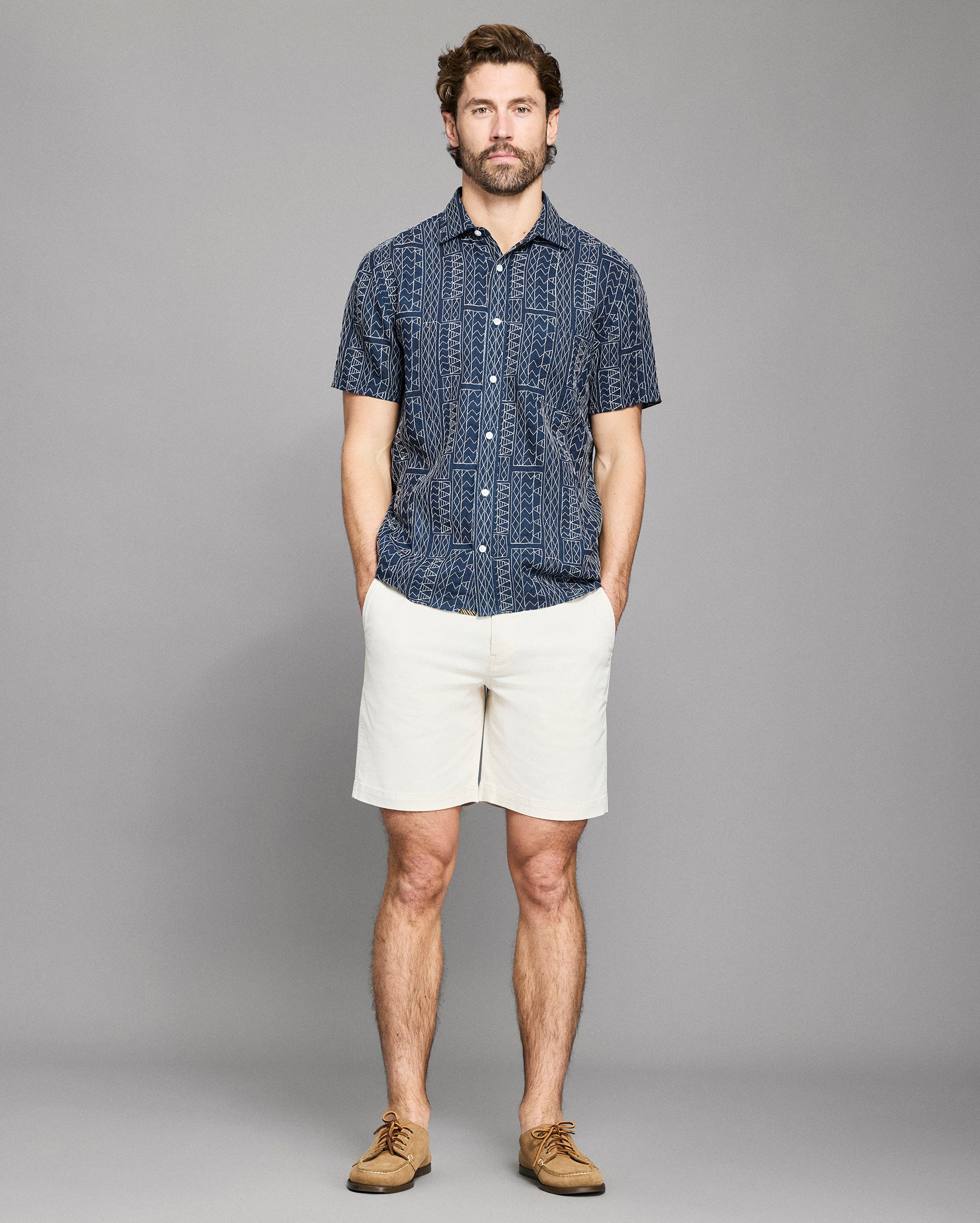 Man wearing a navy patterned shirt and white shorts on a gray background