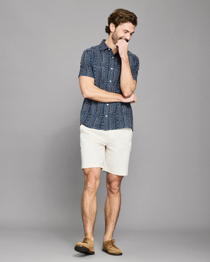 Man wearing a blue patterned shirt and white shorts on a gray background