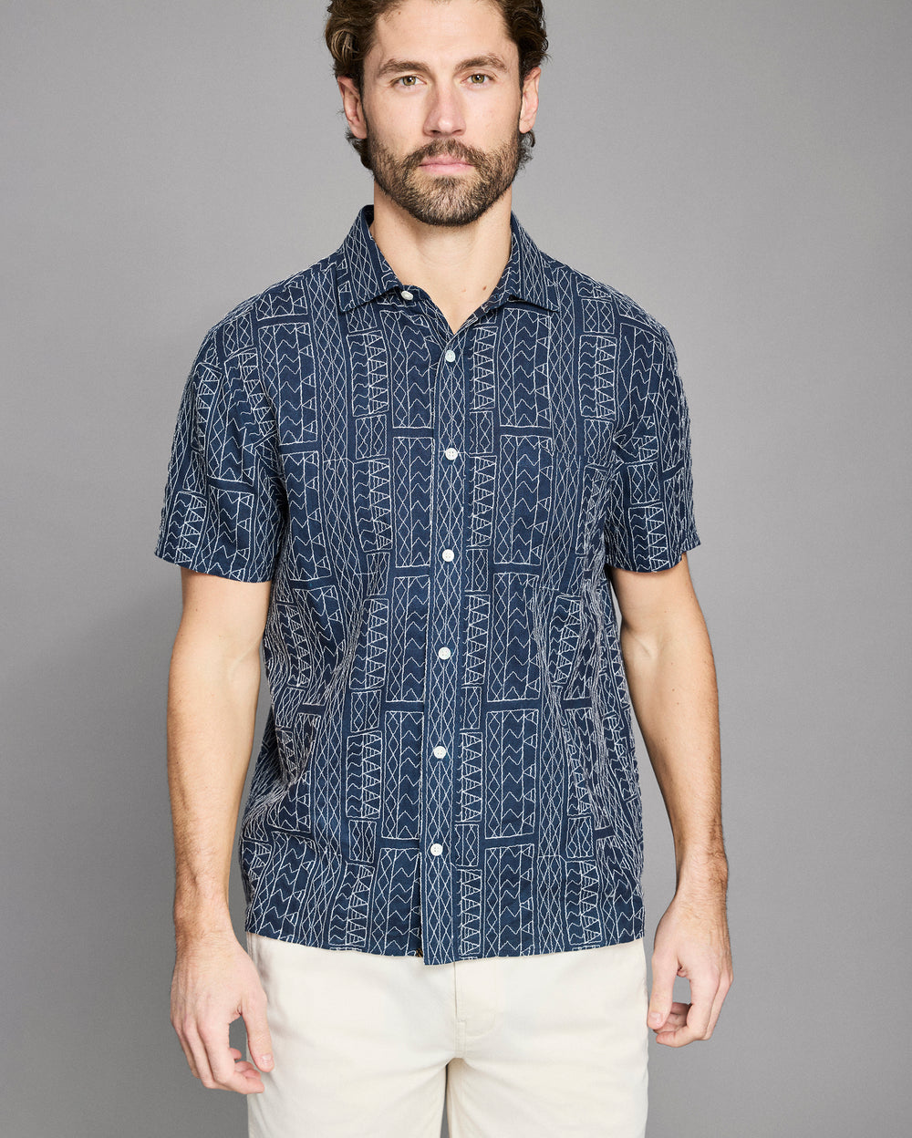 Man wearing a navy patterned shirt against a gray background
