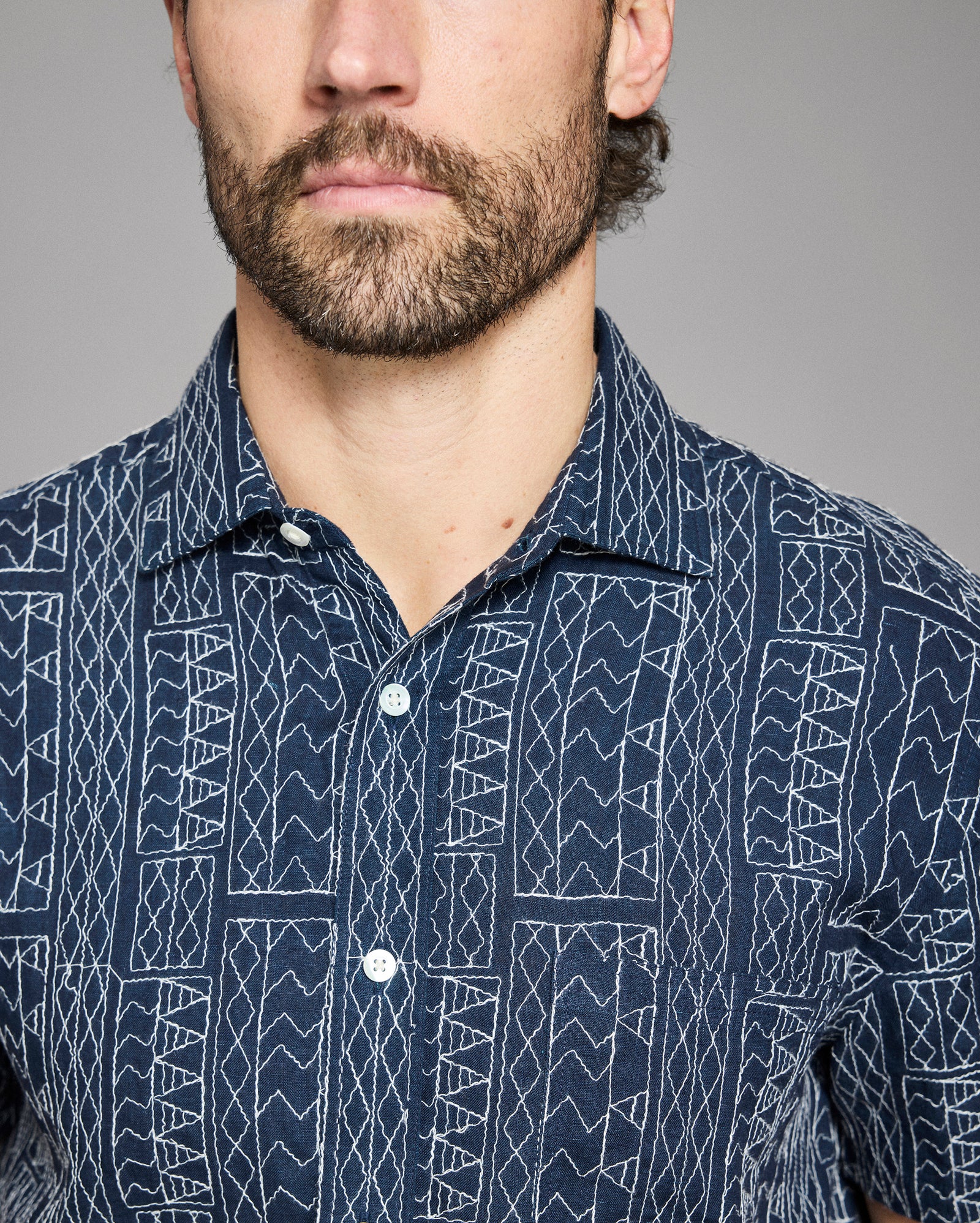 Man wearing a navy blue shirt with white geometric pattern against a gray background