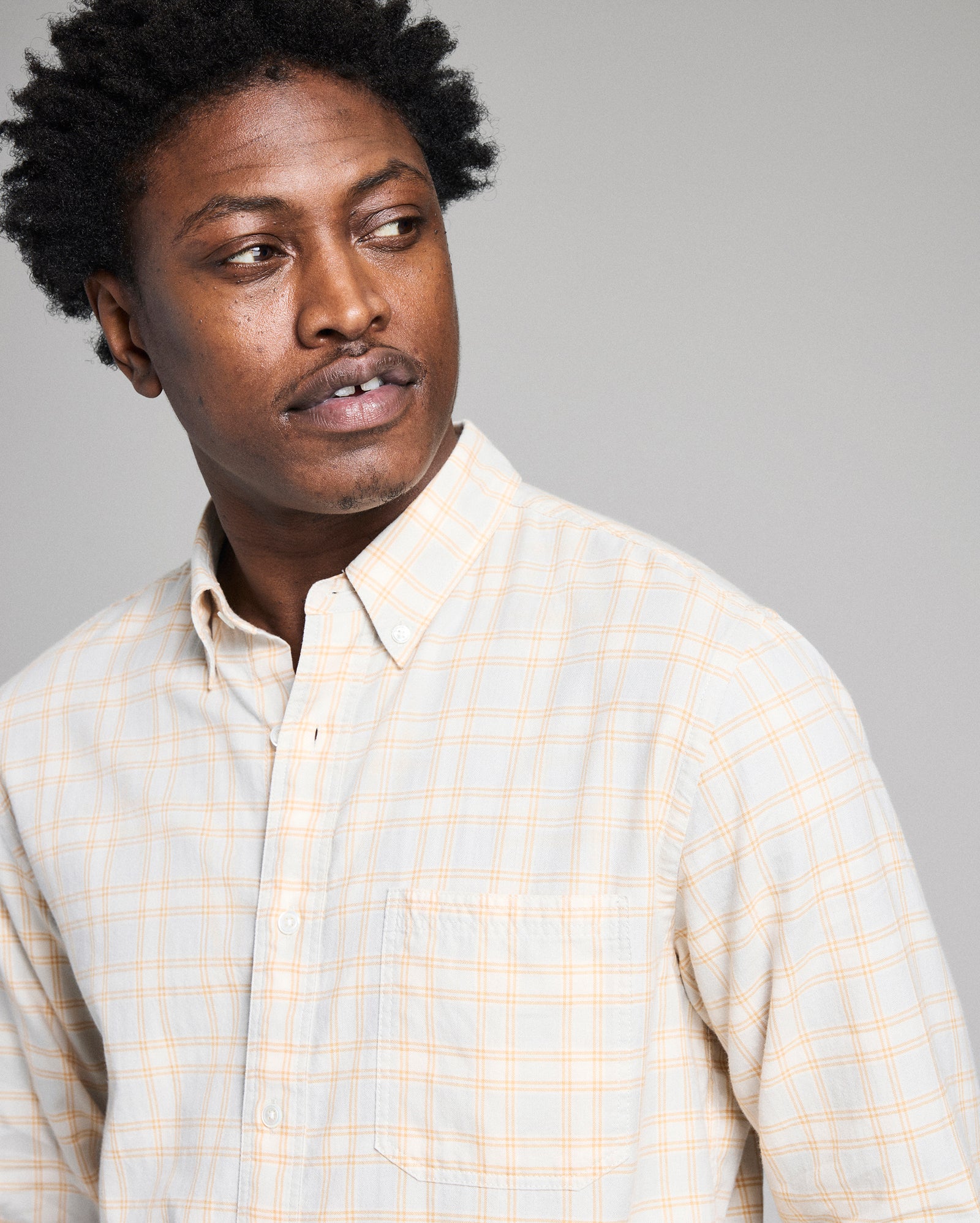 Man wearing a light-colored checkered shirt against a gray background