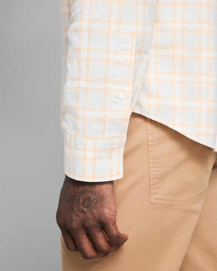 Close-up of a person wearing a white shirt with yellow plaid pattern and beige pants.
