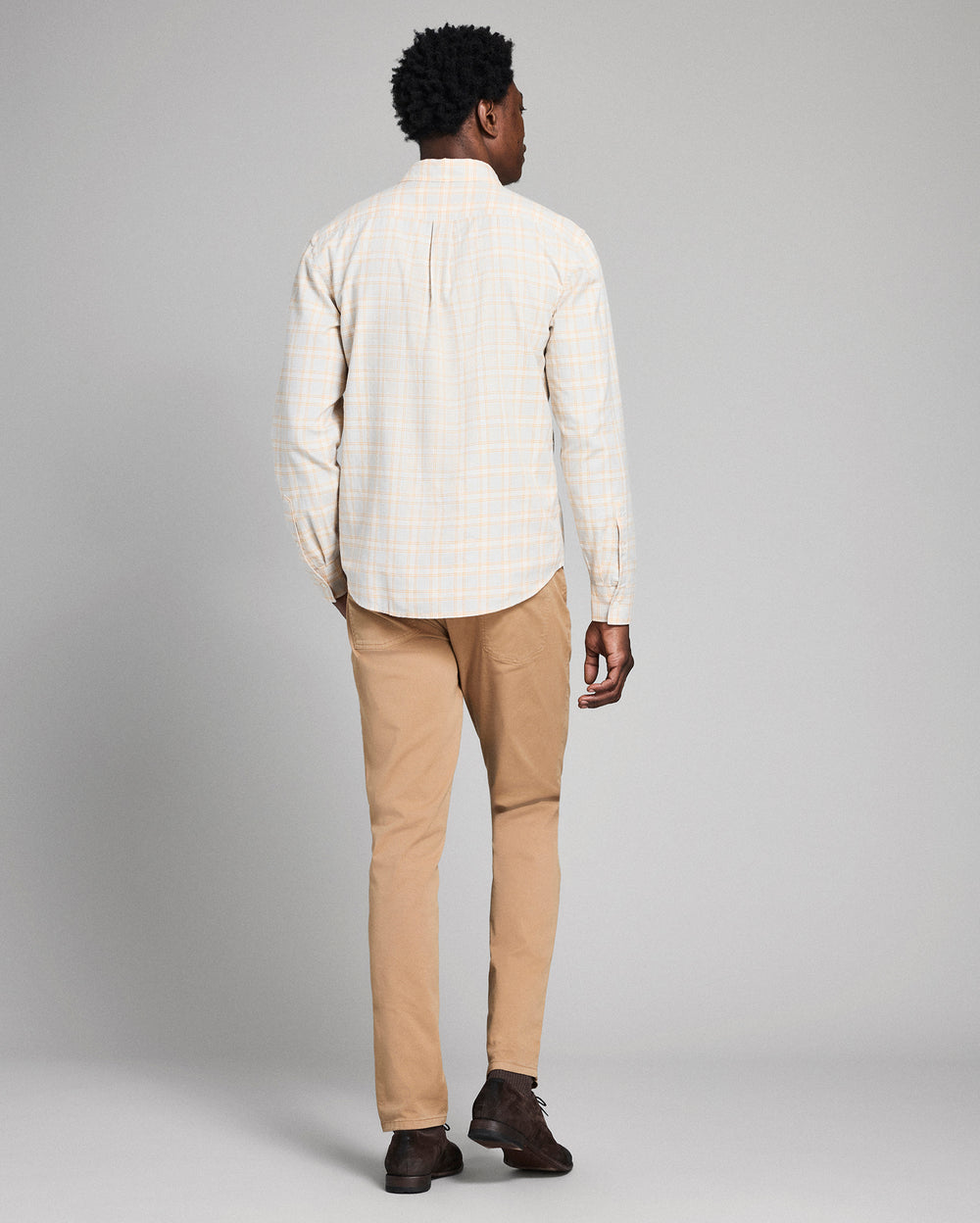 Man wearing a white checkered shirt and beige pants on a gray background