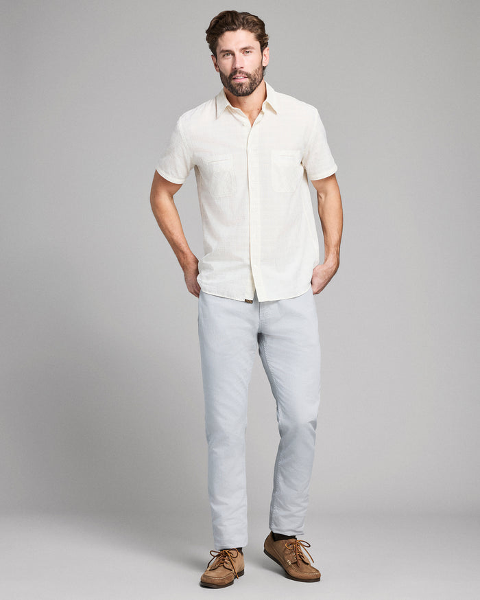 Man wearing a white short-sleeve shirt and light blue jeans on a gray background