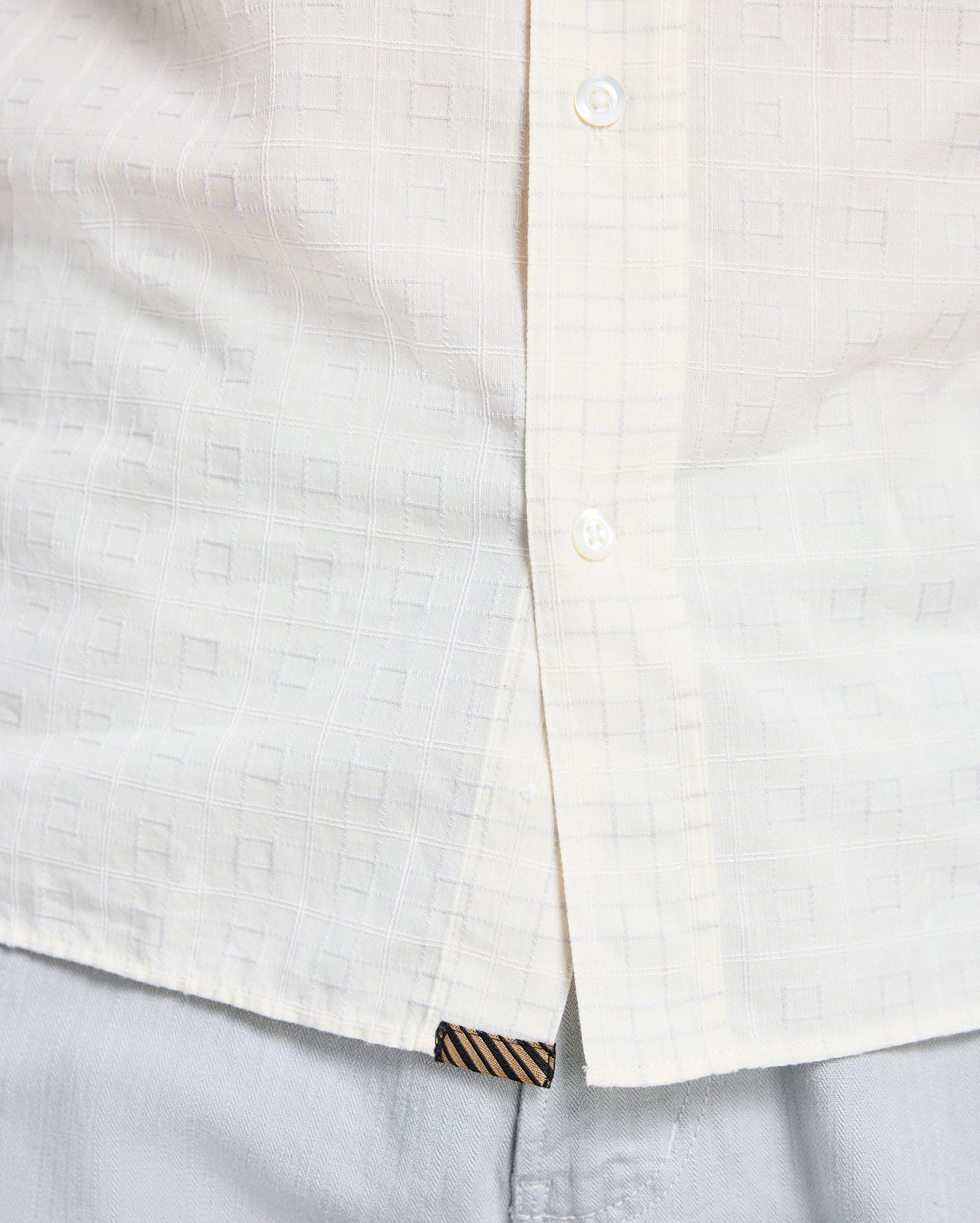 Close-up of a white shirt with a subtle pattern and striped trim on a light gray background