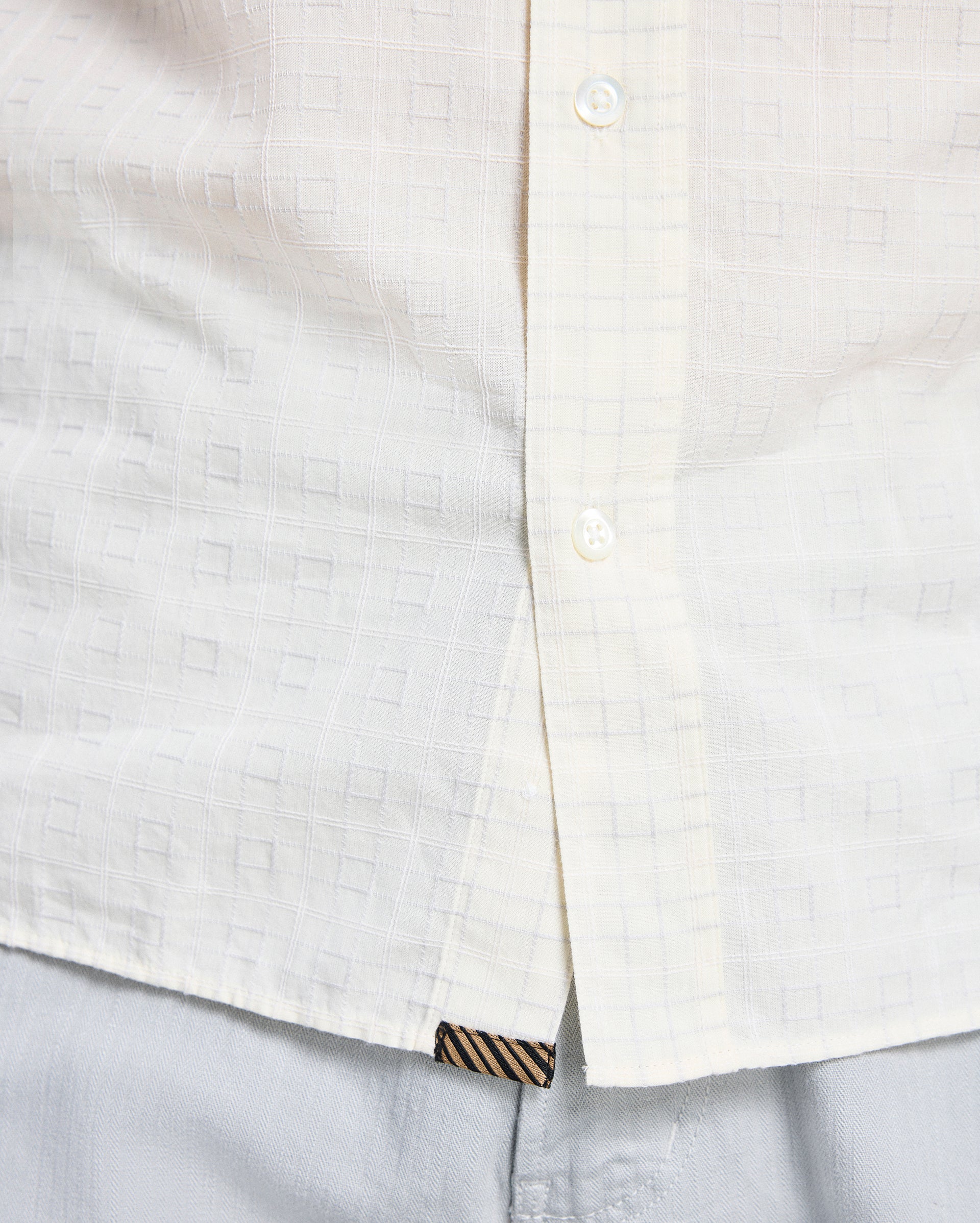 Close-up of a white shirt with a subtle pattern and striped trim on a light gray background