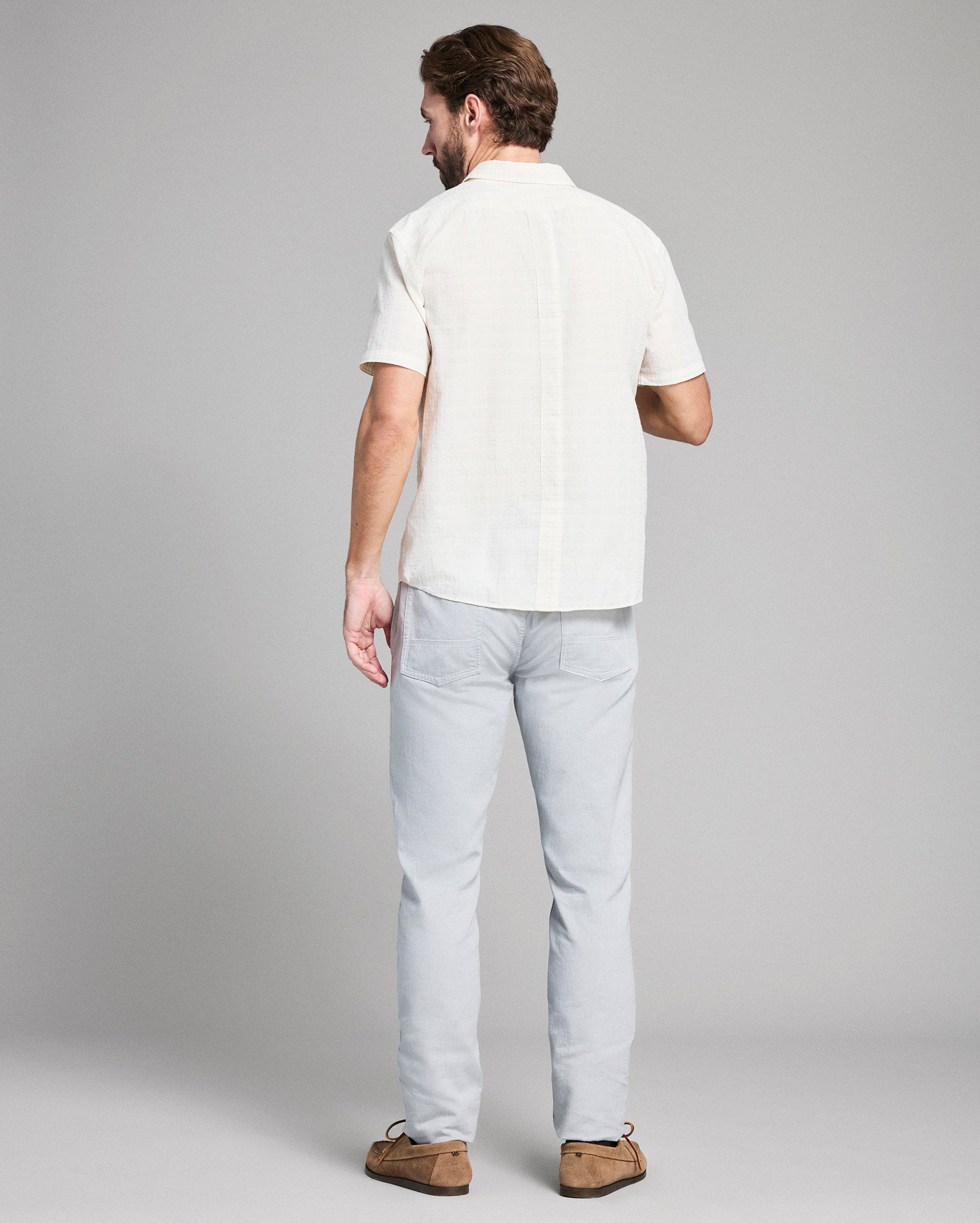 Man wearing a white shirt and light gray pants against a plain background