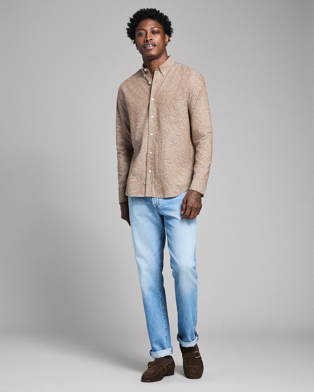 Man wearing a beige shirt and light blue jeans against a gray background