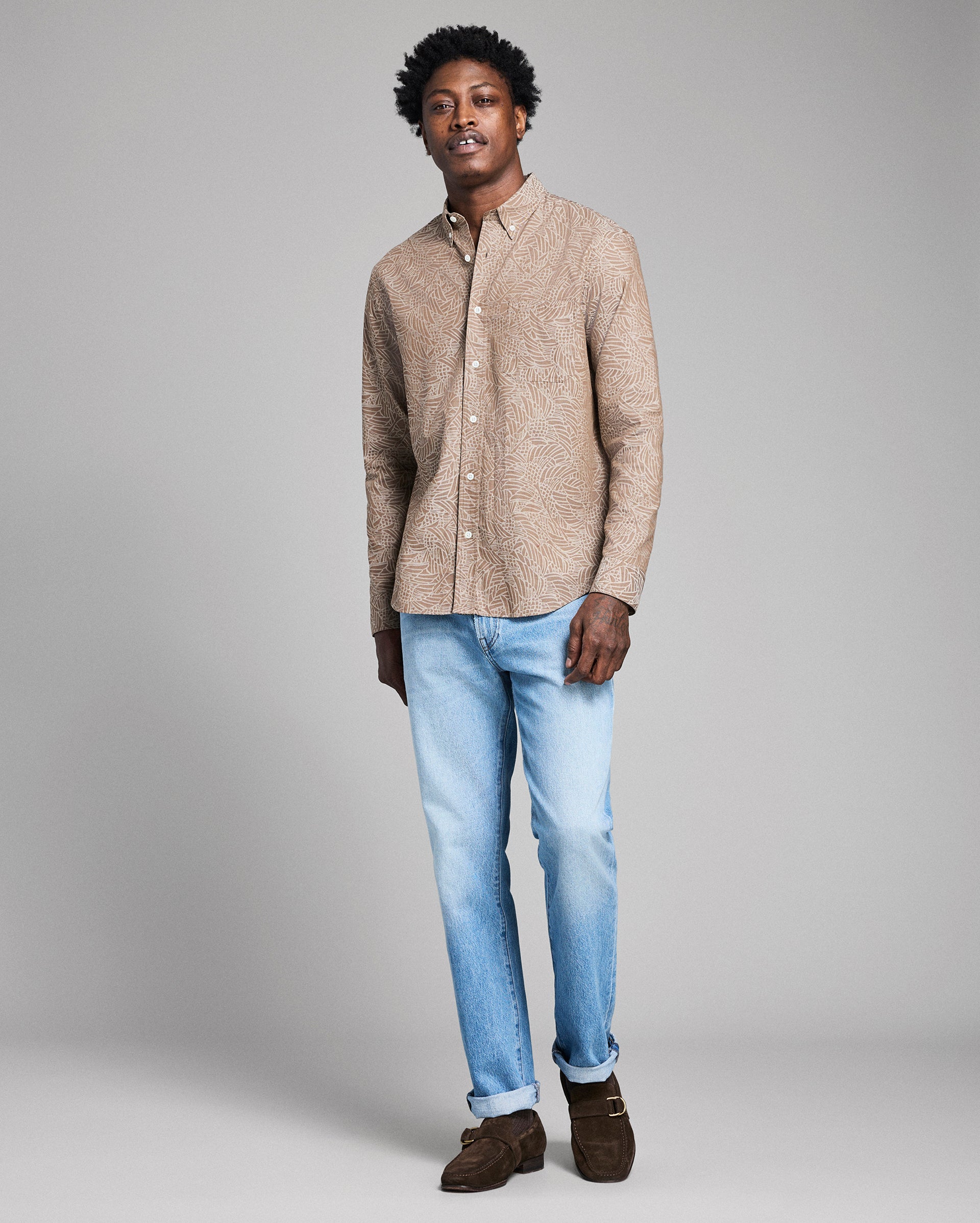 Man wearing a beige shirt and light blue jeans against a gray background