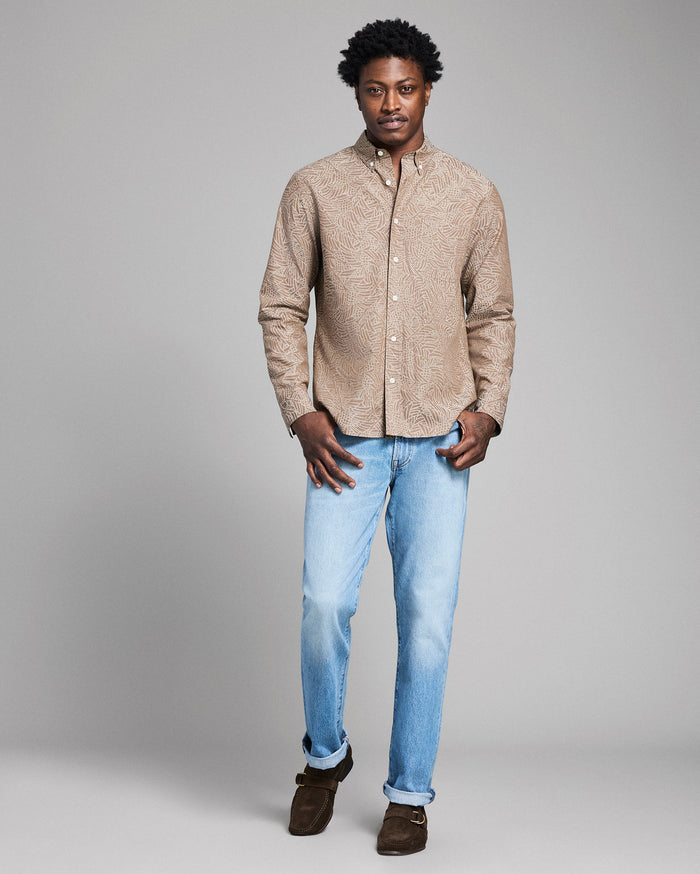 Man wearing a beige textured shirt and light blue jeans on a gray background