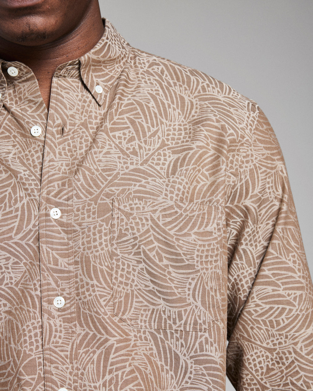 Close-up of a person wearing a patterned beige shirt against a gray background