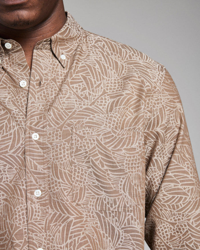 Close-up of a person wearing a patterned beige shirt against a gray background