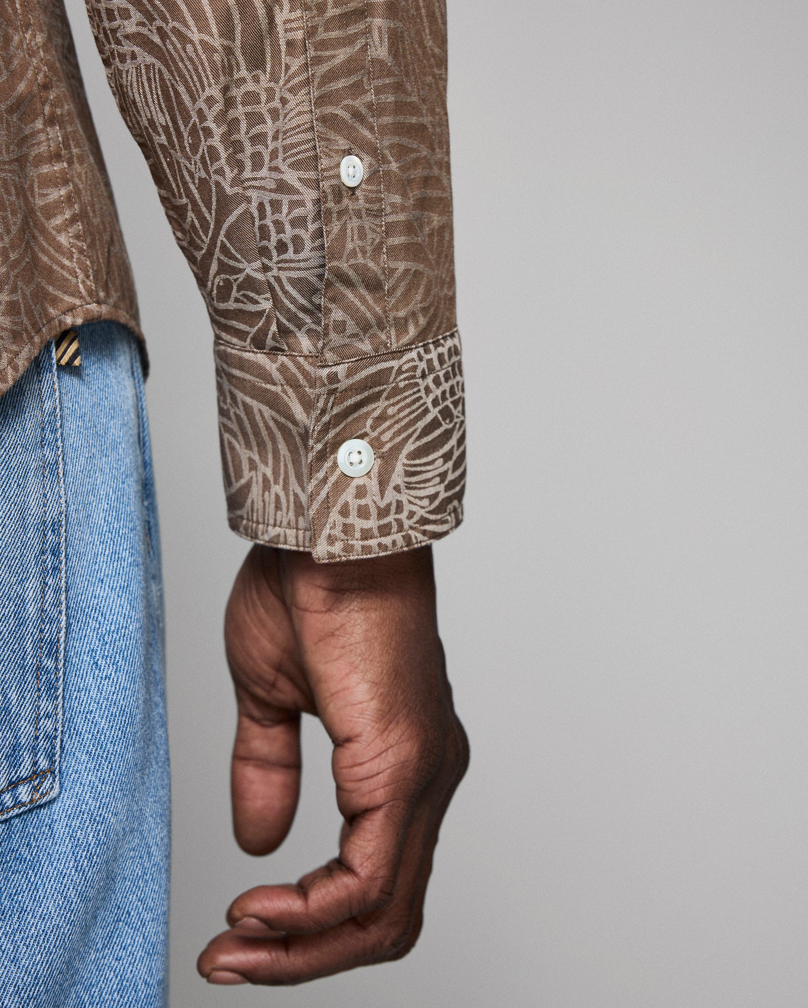 Close-up of a person wearing a patterned shirt and blue jeans on a gray background