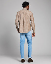 Man wearing a beige patterned shirt and light blue jeans on a gray background