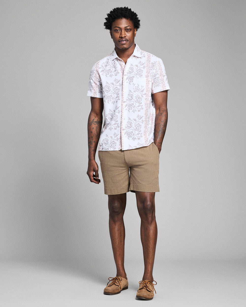 Man wearing a white patterned shirt and beige shorts against a gray background