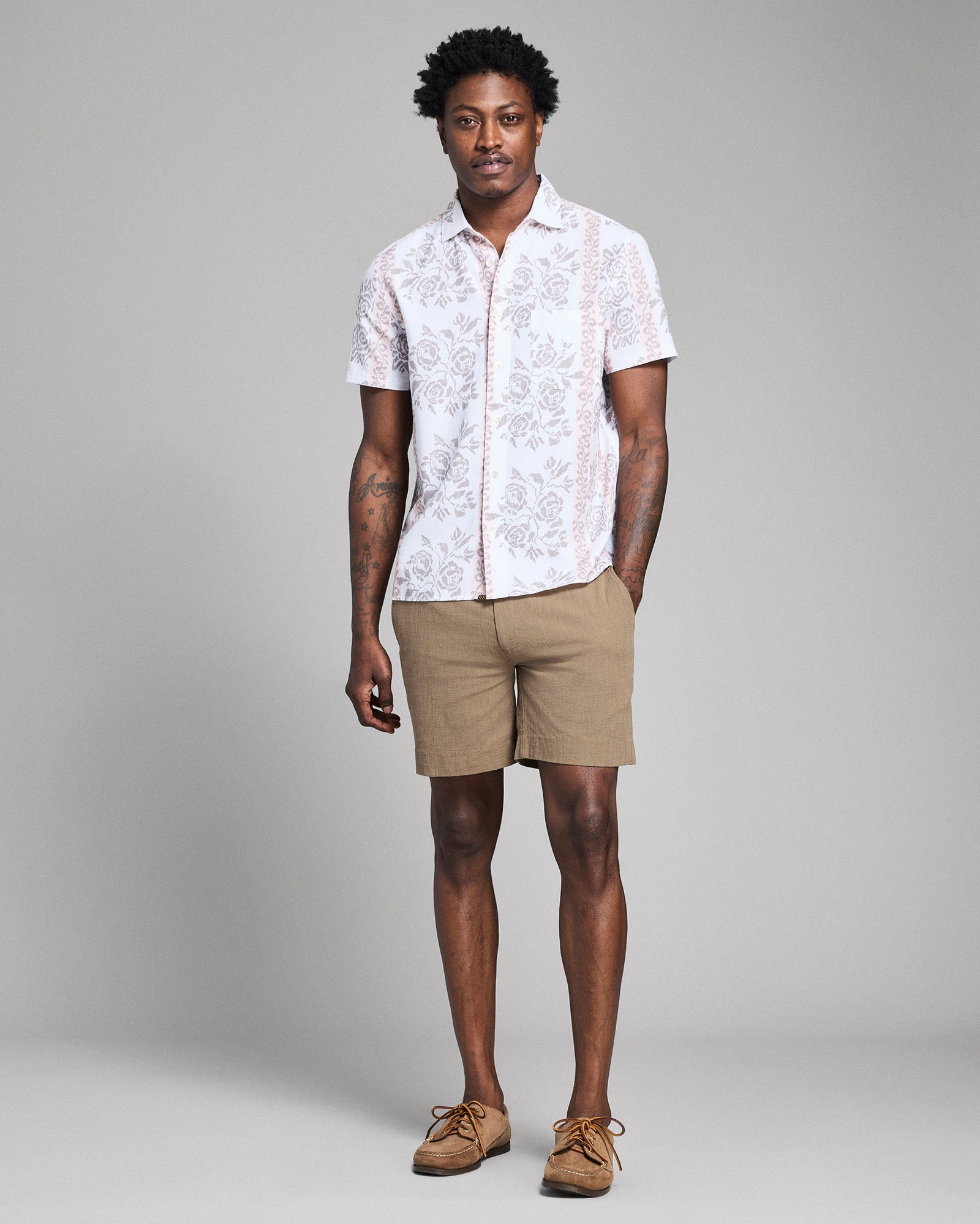 Man wearing a white patterned shirt and beige shorts against a gray background