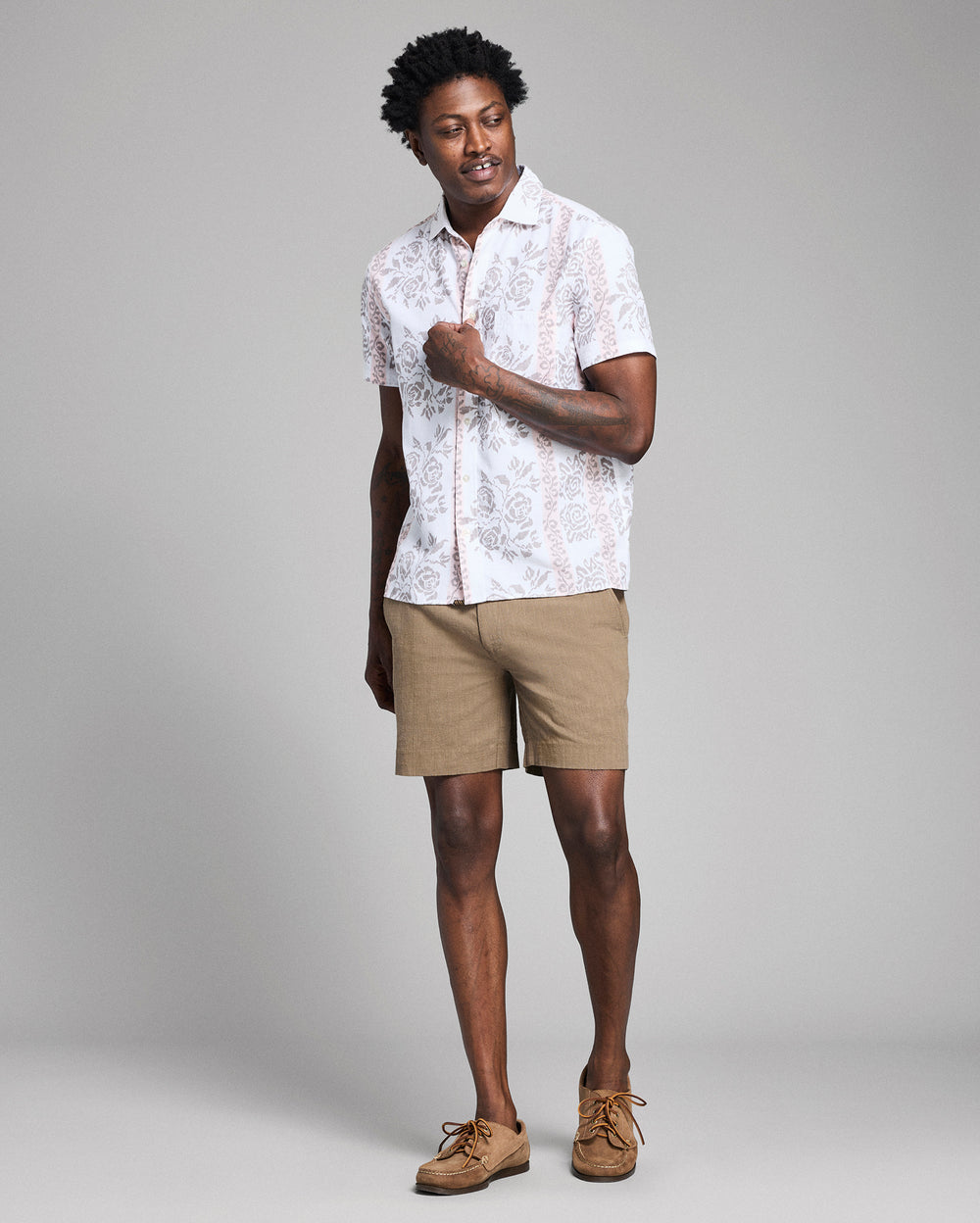 Man wearing a white patterned shirt and beige shorts on a gray background