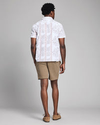 Man wearing a white patterned shirt and beige shorts against a gray background