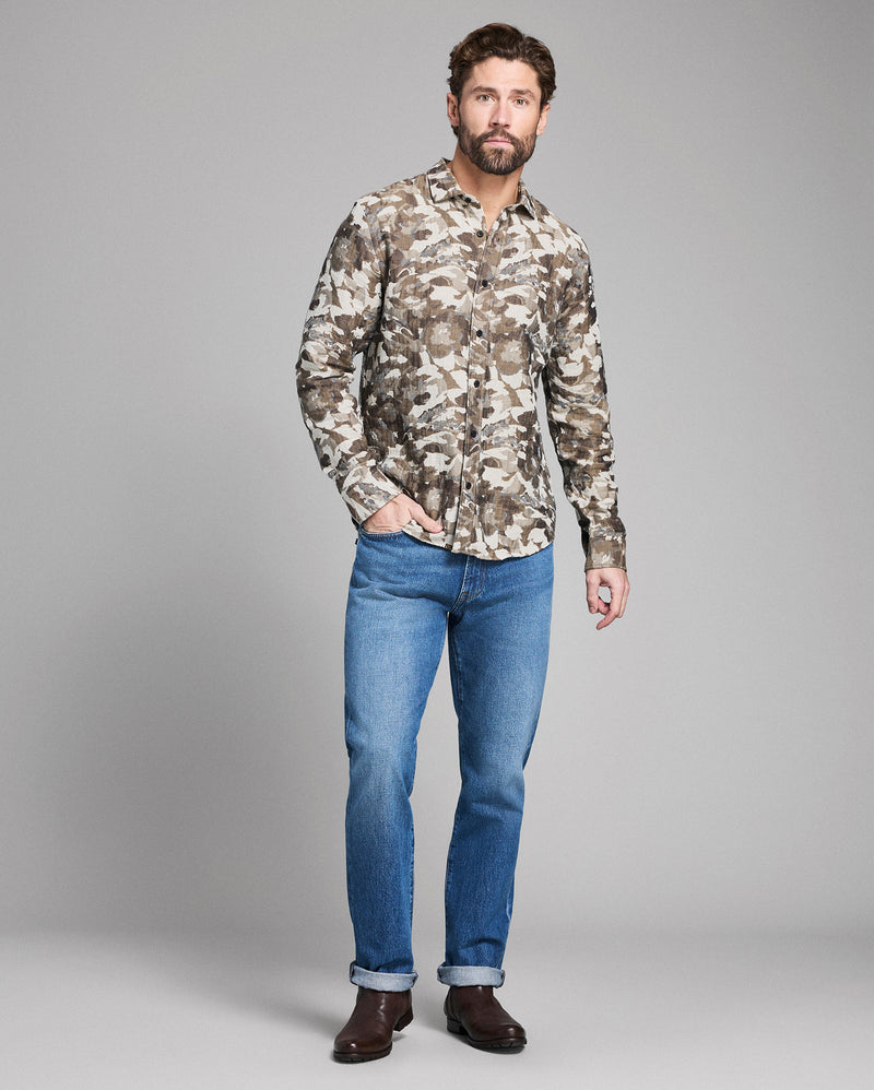 Man wearing a camouflage shirt and blue jeans on a gray background Alternate