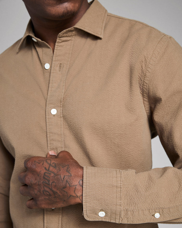 Close-up of a person wearing a beige button-up shirt with a neutral background