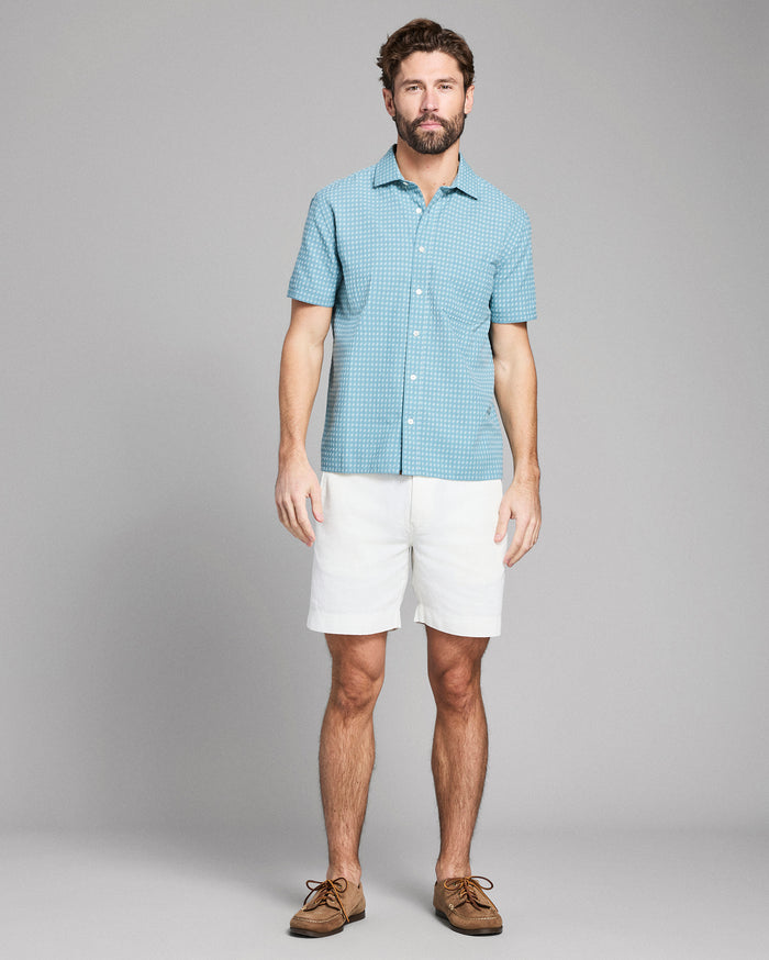 Man wearing a blue checkered shirt and white shorts on a gray background