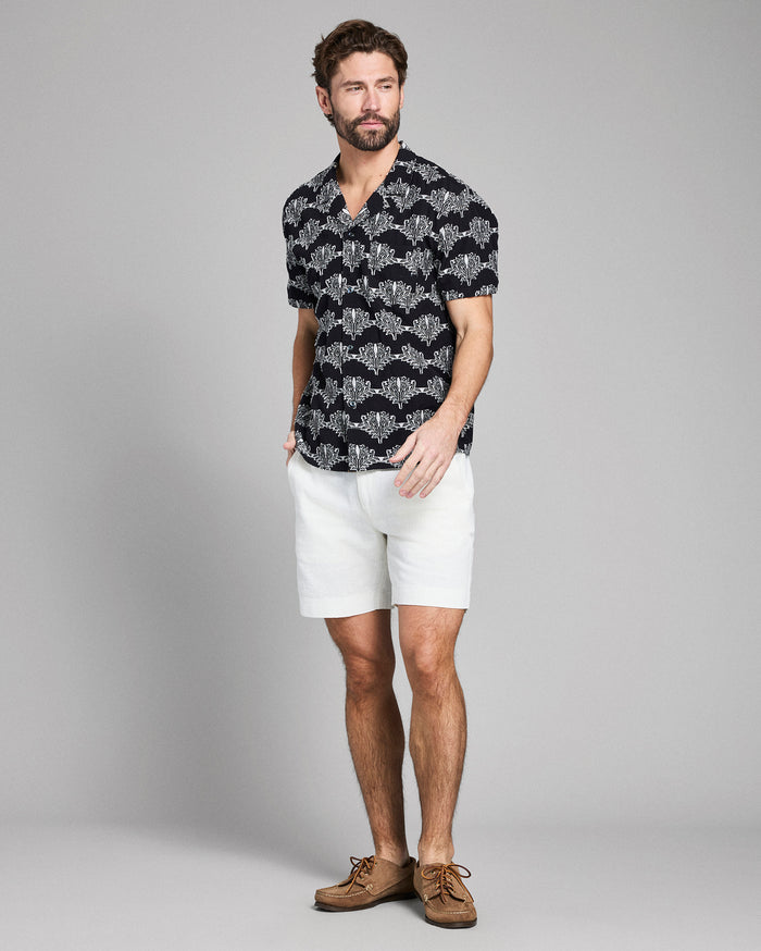 Man wearing a black patterned shirt and white shorts on a gray background
