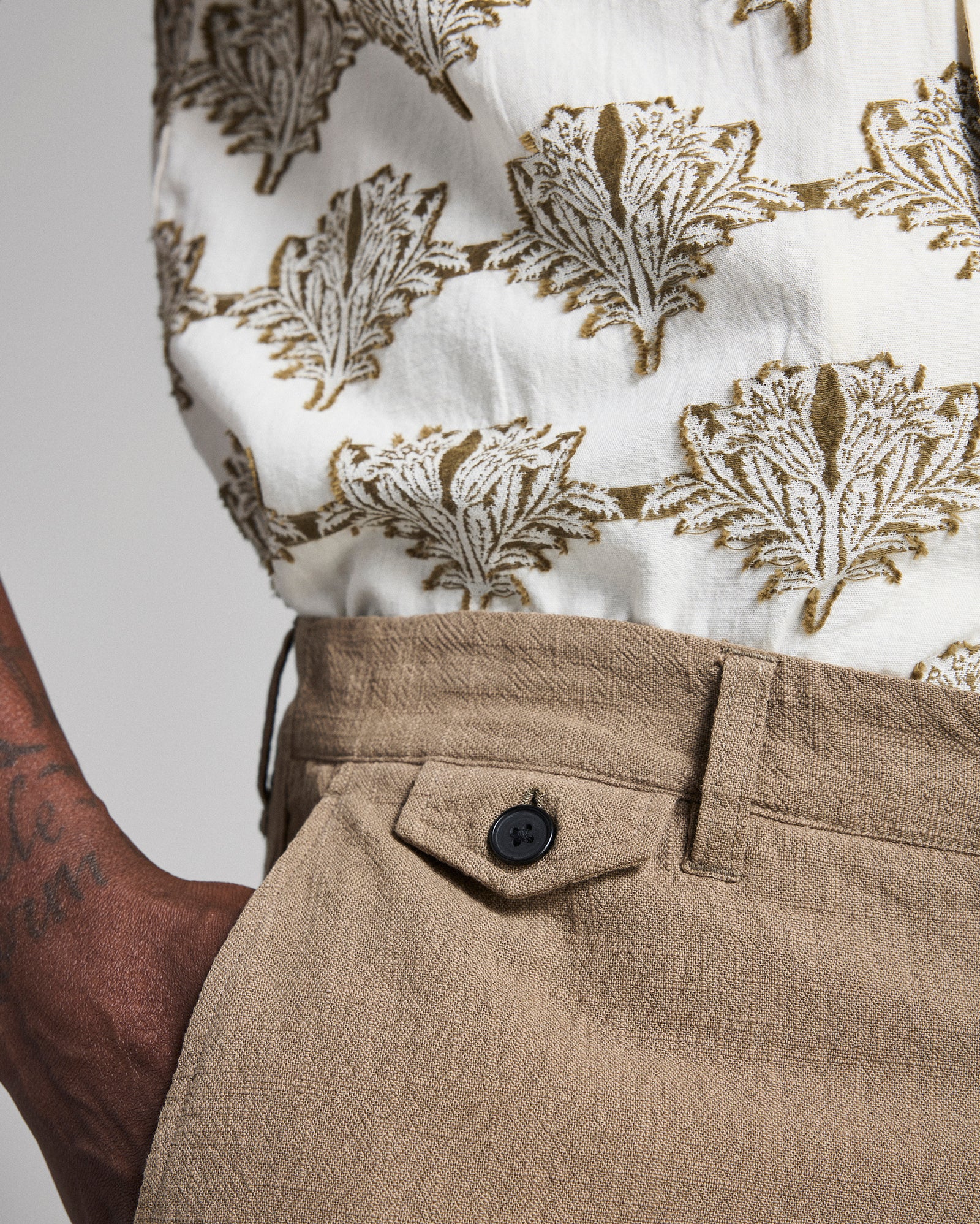 Close-up of a person wearing a white shirt with brown leaf pattern and beige pants.