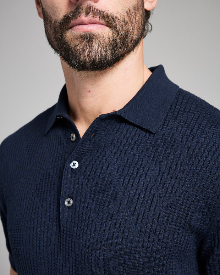 Man wearing a navy blue knitted polo shirt against a gray background